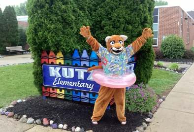  the cougar mascot in a hawaiian shirt with a swim tube in front of the Kutz sign 